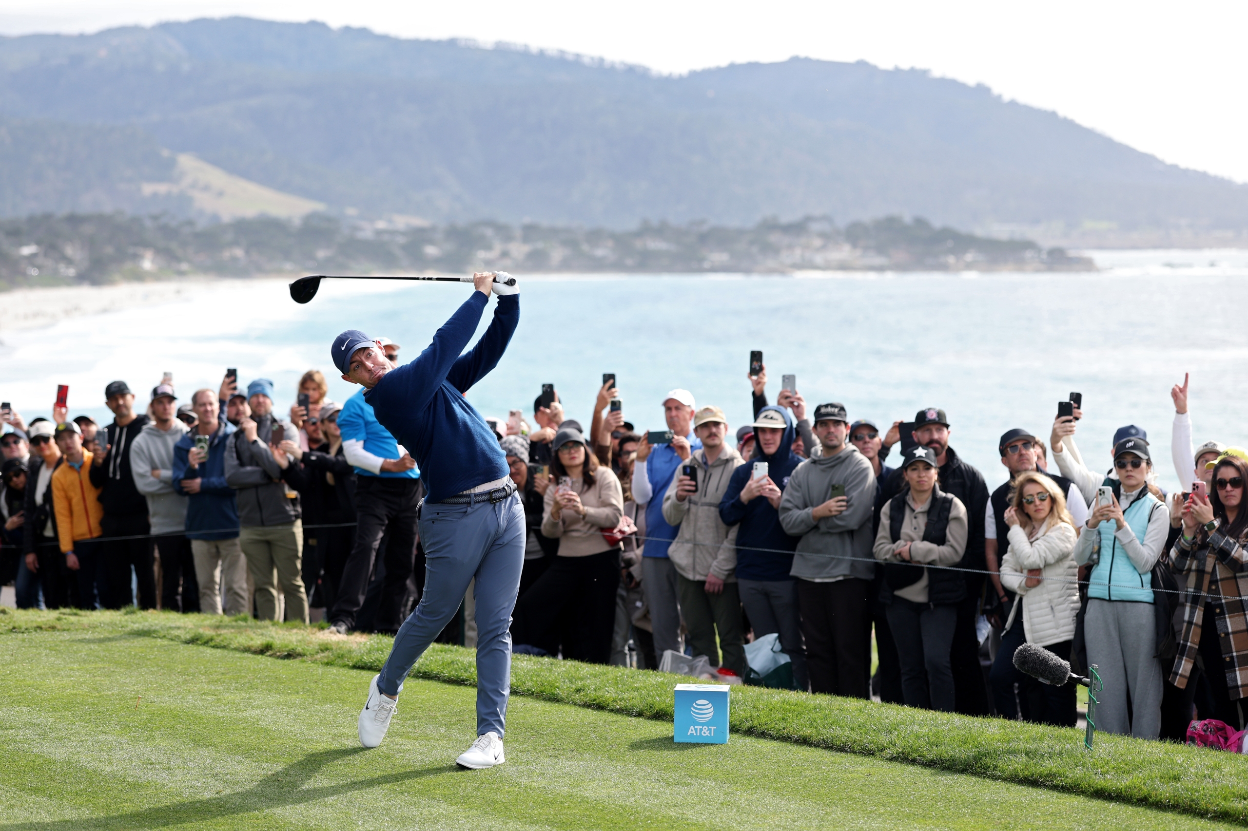 A golfer (likely a celebrity or professional) driving a ball, surrounded by a large gallery of spectators holding up cell phones to take pictures.