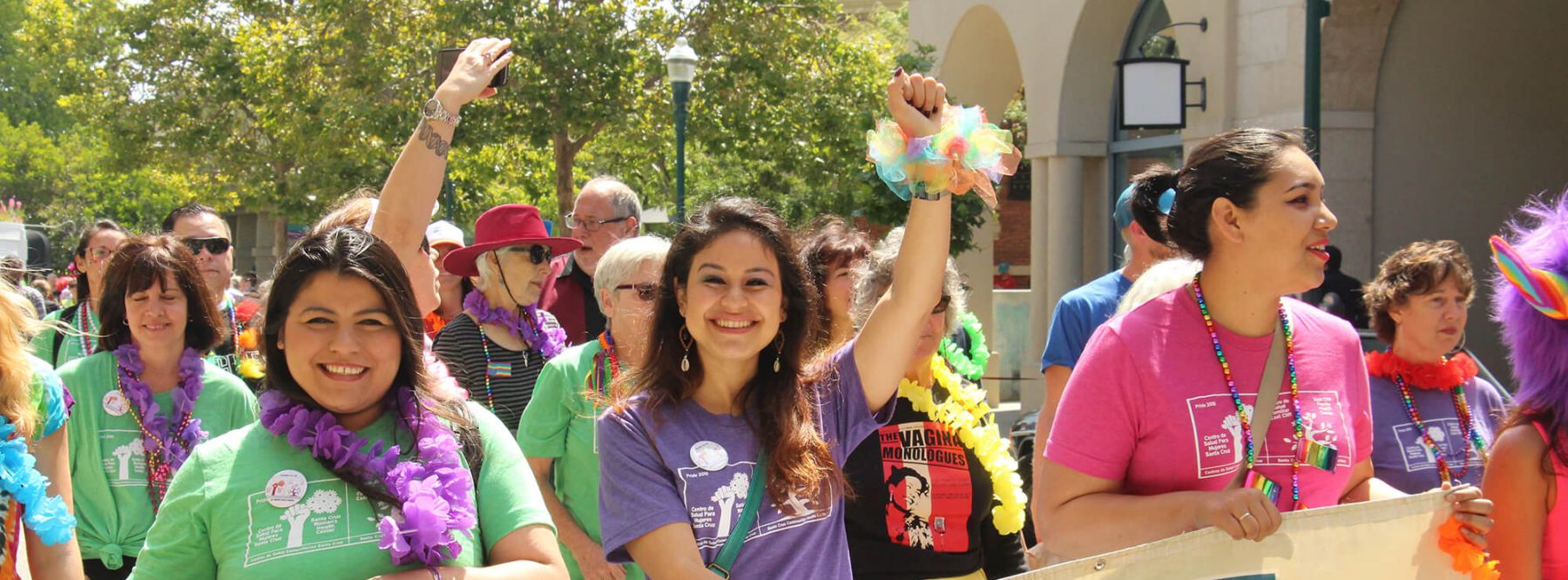 Enthusiastic volunteers and supporters in colorful leis raising their hands while participating in a community pride parade.