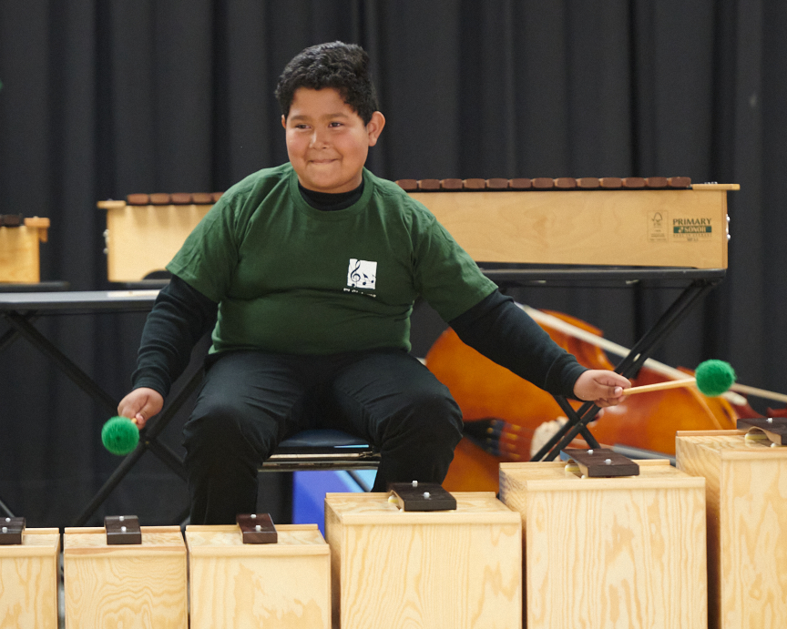 A young student playing a xylophone or marimba during a performance or class, supported by a music education program.