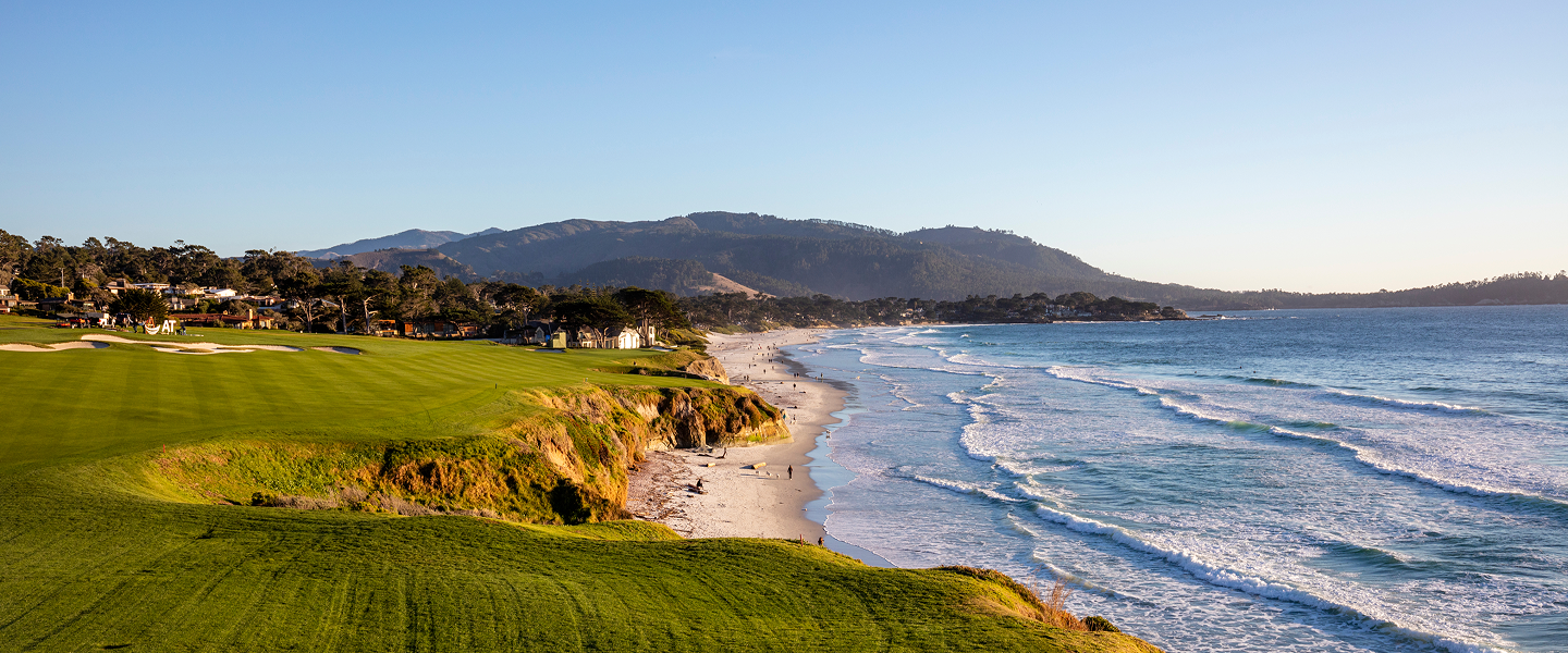 A panoramic coastline view featuring the lush green golf course meeting the sandy beach and ocean waves at Pebble Beach.