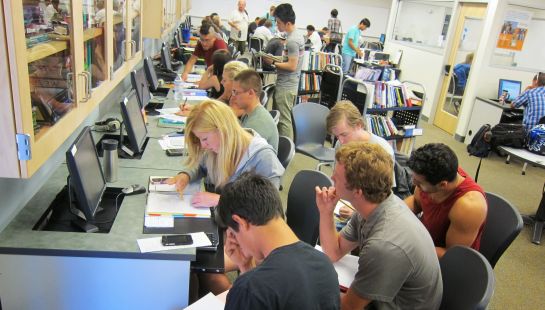 Students working on computers and studying together in a busy classroom or library learning center.