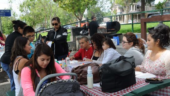 A multi-generational family and community group enjoying a picnic and barbeque outdoors at a park.